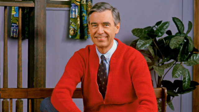 Mister Rogers in a red cardigan and tie on set